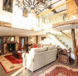 A living room with sofas a fireplace and a staircase with glass railing at The Barn Saham Hills near Swaffham
