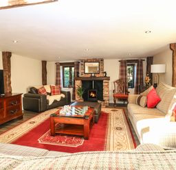 A living room with a fireplace two sofas a chessboard on a wooden table and a large rug at The Barn in Saham Hills near Swaffham