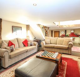 A living room with two sofas a chess board a leather ottoman and a kitchen area at The Barn in Saham Hills near Swaffham