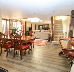 A dining area with wooden table and chairs next to a living room with a sofa and carpet at The Barn in Saham Hills near Swaffham