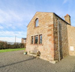 An exterior view of a stone house with a bench and potted plant on a gravel area at Hadrian's View Banks near Brampton
