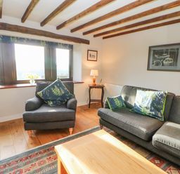 A living room with a dark armchair and sofa with patterned cushions wooden coffee table and exposed wooden ceiling beams at Hadrians View Banks near Brampton