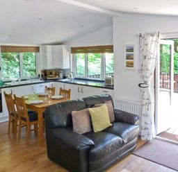 A living area with a black leather sofa and wooden dining table near an open door to a balcony at Top Lodge 4 Skiptory Howe White Cross Bay near Troutbeck Bridge