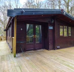 A wooden cabin with a deck and railing surrounded by trees at Top Lodge 4 Skiptory Howe White Cross Bay near Troutbeck Bridge