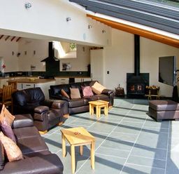 A living area with brown leather sofas wooden tables wood burning stove and dining table at Garth Morthin The Barn in Porthmadog