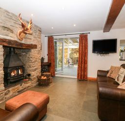 A living room with a stone fireplace a mounted deer head and brown leather sofas at Garth Morthin The Stables in Porthmadog