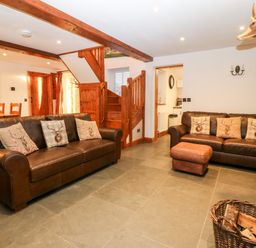 A living room with two leather sofas wooden staircase and a stone fireplace at Garth Morthin The Stables in Porthmadog