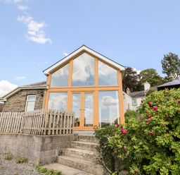 A stone house with large glass windows and wooden frames stairs and bushes outside at Llety'r Wennol Ffarmers near Lampeter