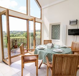 A dining area with wooden chairs and a table with a polka dot tablecloth near large glass doors at Llety'r Wennol in Ffarmers near Lampeter