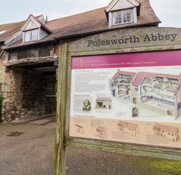 An information board about Polesworth Abbey in front of a stone and brick building with an archway at Polesworth Abbey in Polesworth