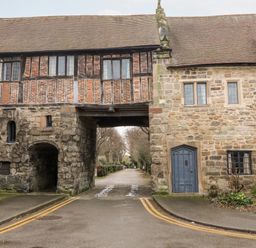 An old stone and brick building with an archway and a road passing underneath at Porters Lodge in Polesworth
