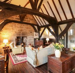 A living room with wooden beams stone fireplace sofa armchair and wooden furniture at Porters Lodge in Polesworth