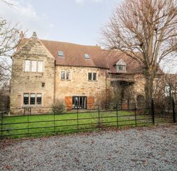 A stone house with a pitched roof and multiple windows behind a black metal fence and a gravel area at Gatehouse Croft in Polesworth