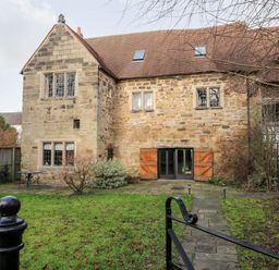A stone house with wooden shutters on the windows and a tiled roof with a garden and a paved path at Gatehouse Croft in Polesworth
