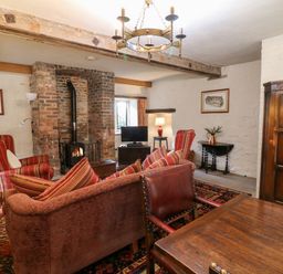 A living room with a wood burning stove a sofa armchairs and a wooden dining table with a red candle at Gatehouse Croft Polesworth
