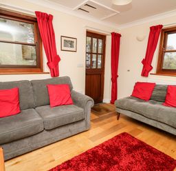 A sitting room with two grey sofas with red cushions and red curtains at Penlon in Capel Bangor near Aberystwyth