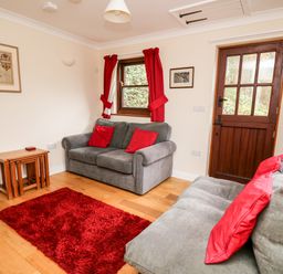 A living room with two gray sofas with red cushions a red rug wooden tables red curtains and a wooden door at Penlon in Capel Bangor near Aberystwyth