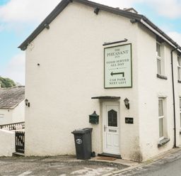Exterior of a white building with a door and a sign for The Pheasant Inn in a small village