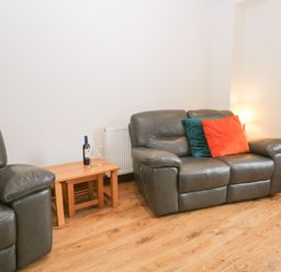 A living room with two leather sofas a wooden side table with a bottle of wine and two glasses at Fernleigh Cottage in Allithwaite near Grange-over-Sands