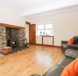A living room with a stone fireplace wooden floor brown door leather sofas and colorful cushions at Fernleigh Cottage in Allithwaite near Grange-over-Sands