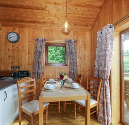 A wooden dining area with a table set for four near a kitchen countertop and large window at Barn Shelley Lodge in Copplestone near Crediton