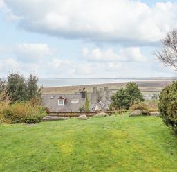 A grassy garden with bushes and trees overlooking rooftops and a castle with a coastline in the background at The Villa in Harlech