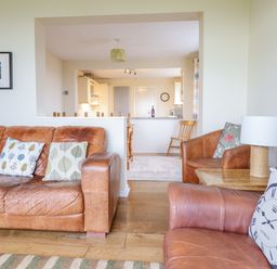 A living room with brown leather sofas and pillows and a wooden side table with a lamp at The Villa in Harlech