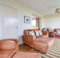 A living room with brown leather sofas cushions a wooden side table lamp and a striped rug at The Villa in Harlech