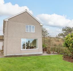 Exterior view of a two-story house with a grass lawn and wooden fence at The Villa in Harlech