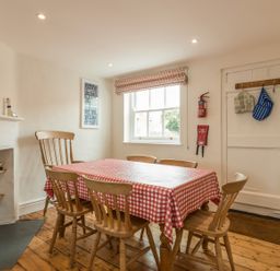 A dining room with a table covered by a red and white checkered tablecloth and six wooden chairs at 3B Coastguard Cottages in Low Newton-By-The-Sea