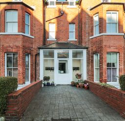 Entrance to a red brick building with potted plants on either side of a paved walkway at Carisbrooke House Apartment 6 in Scarborough
