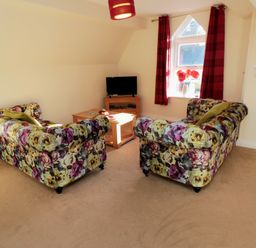 A sitting area with floral patterned sofas, a wooden coffee table, a small TV on a stand, and a window with red curtains at Carisbrooke House, Apartment 6 in Scarborough