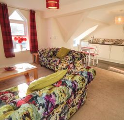 A living room with floral sofas a wooden coffee table and a kitchen area at Carisbrooke House Apartment 6 in Scarborough
