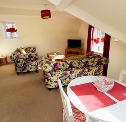 A living room with floral sofas a small tv on a wooden stand a coffee table and a dining table with red placemats at Carisbrooke House Apartment 6 in Scarborough