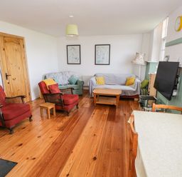 A living room with two red armchairs green and gray sofas wooden coffee table TV on wall and dining table at The Old School House in Gortermone near Carrigallen County Leitrim