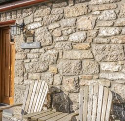 A stone wall with a wooden door and two wooden chairs outside at Hen Stabl Llangoed near Beaumaris