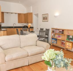 A living room and kitchen area with beige sofa dining table with chairs and bookshelf at Hen Stabl in Llangoed near Beaumaris