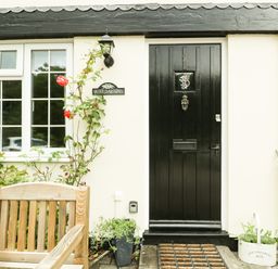 The entrance of a house with a black door and window beside wooden chair and plants at Wye Valley Cottage in Symonds Yat