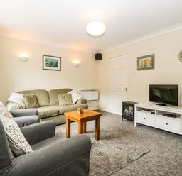 A living room with green sofa gray armchairs wooden coffee table television and white cabinet at Wye Valley Cottage Symonds Yat