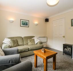 A living room with a green sofa grey armchairs wooden coffee table and electric fireplace at Wye Valley Cottage in Symonds Yat