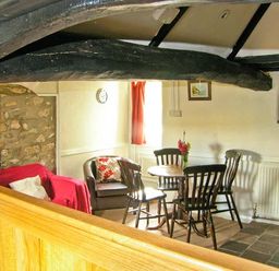 A dining area with a round wooden table surrounded by four chairs and a sitting area with a red armchair and a brown armchair at Gorrig Bwthyn in Llandysul