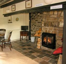 A room with a stone fireplace with firewood and a fire a wooden dining table with chairs and a small television on a stand at Gorrig Bwthyn in Llandysul