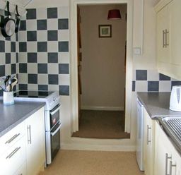 A kitchen with checkered tile walls stove sink kettle and kitchen utensils at Gorrig Bwthyn in Llandysul