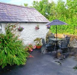 An outdoor patio with a table umbrella chairs and plants beside a white stone wall at Gorrig Bwthyn in Llandysul