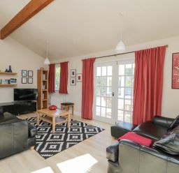 A living room with black leather sofas a wooden coffee table and red curtains at Orchard Lodge in Warkworth