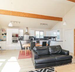 A kitchen and dining area with white cabinets a round wooden dining table with black chairs and a black sofa at Orchard Lodge in Warkworth