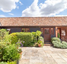 An outdoor patio area with plants and shrubs in front of a building with a tiled roof at Horseshoe in Little Glemham near Wickham Market
