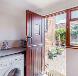 A utility room with a washing machine an iron basket and a wooden door opening to a garden at Horseshoe in Little Glemham near Wickham Market