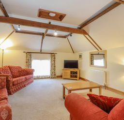 A living room with red patterned sofas a wooden coffee table a television on a wooden stand and exposed wooden ceiling beams at Hayloft Cottage in Little Glemham near Wickham Market
