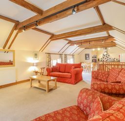 A sitting area with red sofas and a wooden coffee table in a room with exposed wooden beams at Hayloft Cottage in Little Glemham near Wickham Market